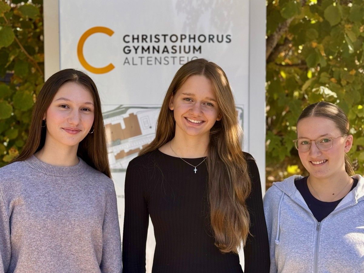 Drei junge Frauen stehen vor einem Schild mit der Aufschrift „Christophorus Gymnasium Altensteig“.